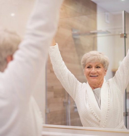 Senior woman joyfully checking out her dental implants in bathroom mirror